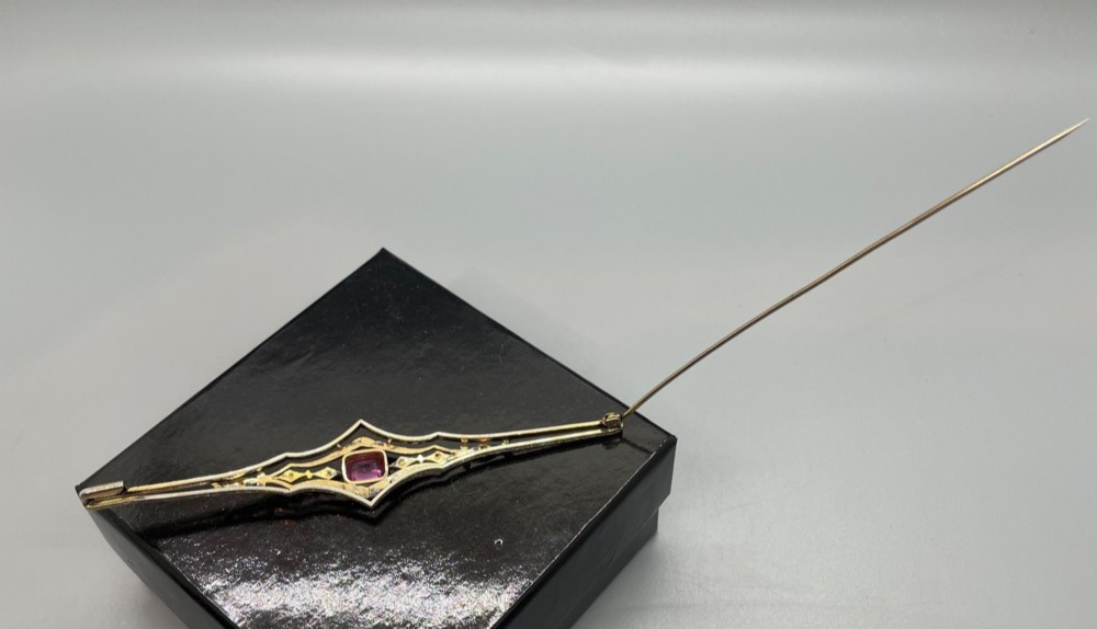 An Edwardian silver gilt bar brooch featuring geometric openwork filigree and a central cushion-cut pink paste stone. View XII