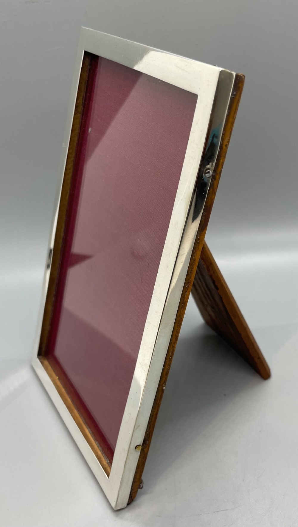 An upright rectangular sterling silver photo frame with a polished border, easel back stand, and burgundy fabric interior. View III