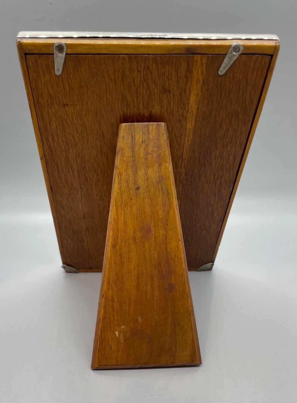 An upright rectangular sterling silver photo frame with a polished border, easel back stand, and burgundy fabric interior. View V