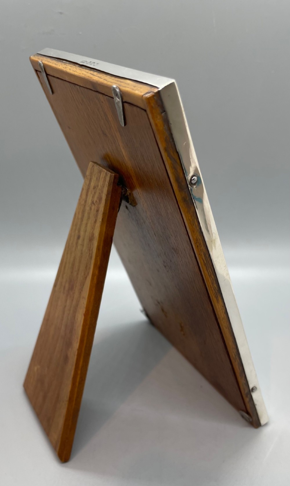 An upright rectangular sterling silver photo frame with a polished border, easel back stand, and burgundy fabric interior. View VI