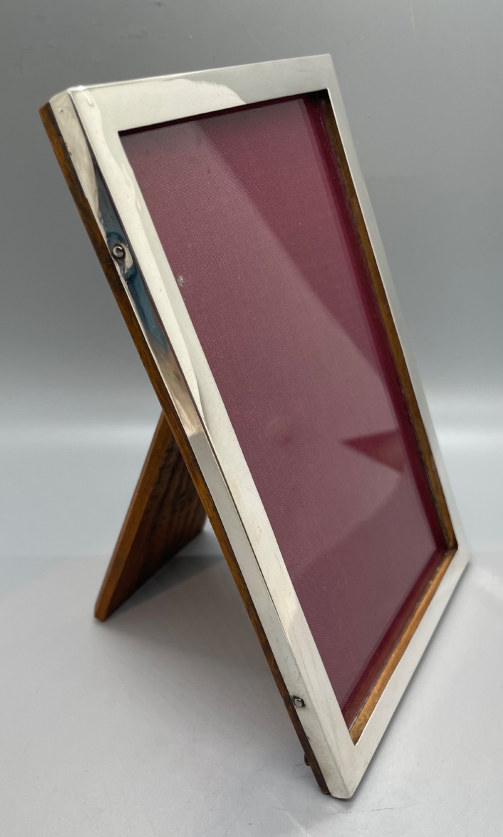An upright rectangular sterling silver photo frame with a polished border, easel back stand, and burgundy fabric interior. View VII