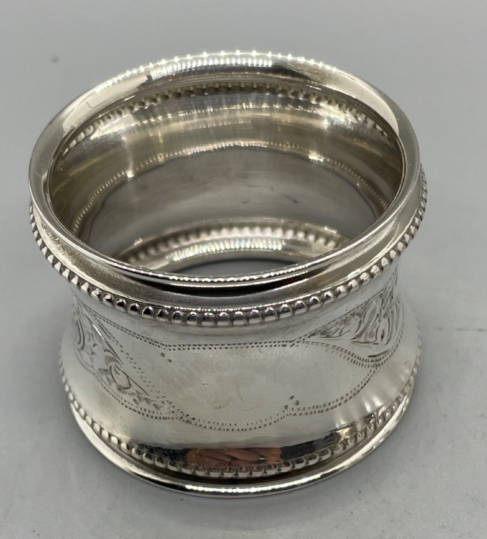 A set of six circular Edwardian sterling silver napkin rings with engraved patterns, displayed inside an open presentation box with green velvet lining. View VI