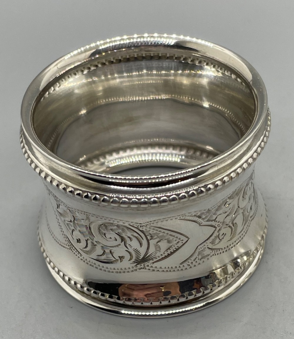 A set of six circular Edwardian sterling silver napkin rings with engraved patterns, displayed inside an open presentation box with green velvet lining. View VII
