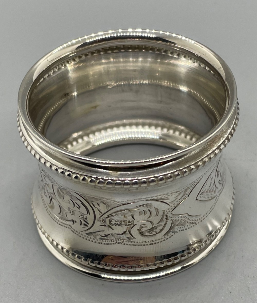 A set of six circular Edwardian sterling silver napkin rings with engraved patterns, displayed inside an open presentation box with green velvet lining. View VIII
