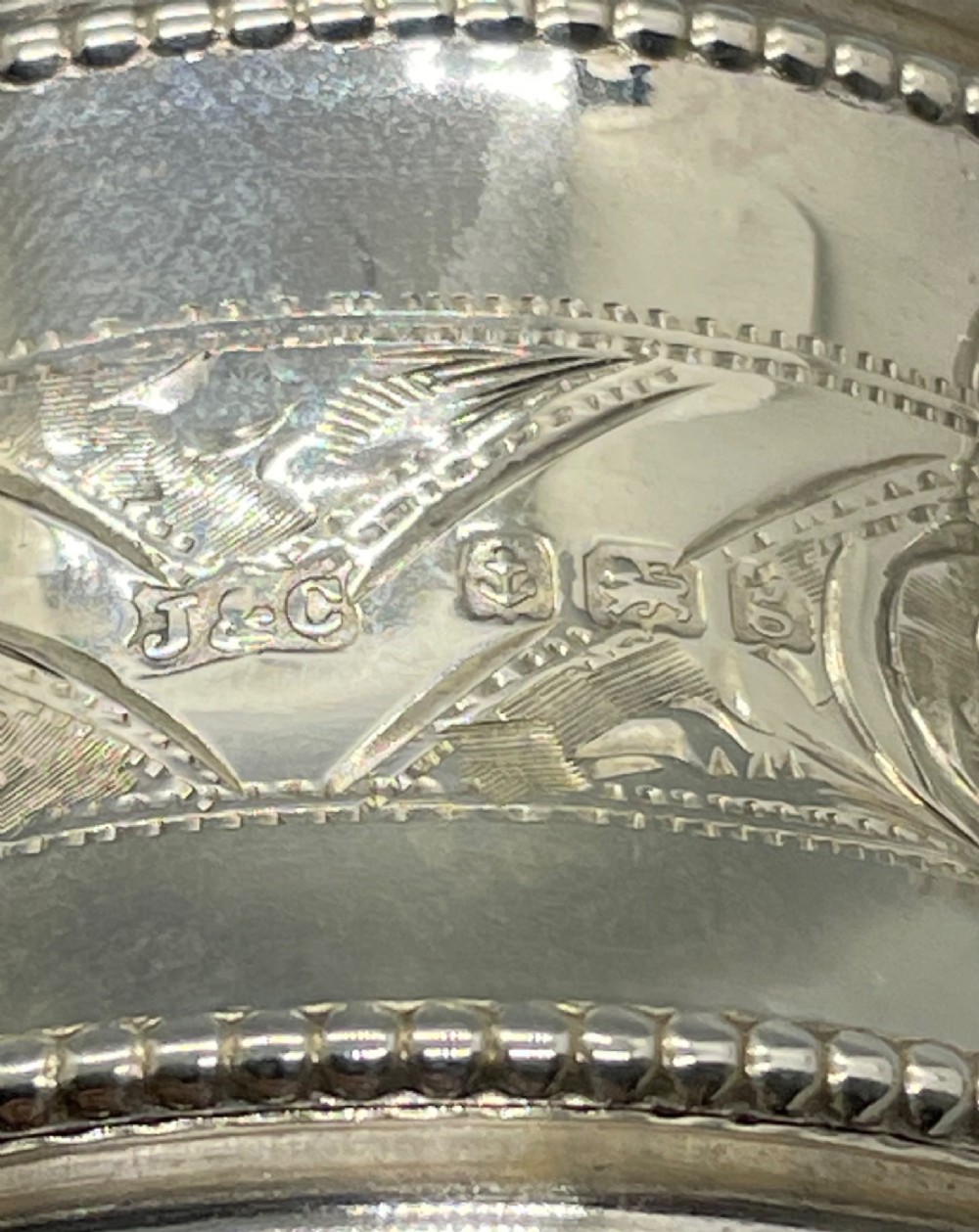 A set of six circular Edwardian sterling silver napkin rings with engraved patterns, displayed inside an open presentation box with green velvet lining. View IX