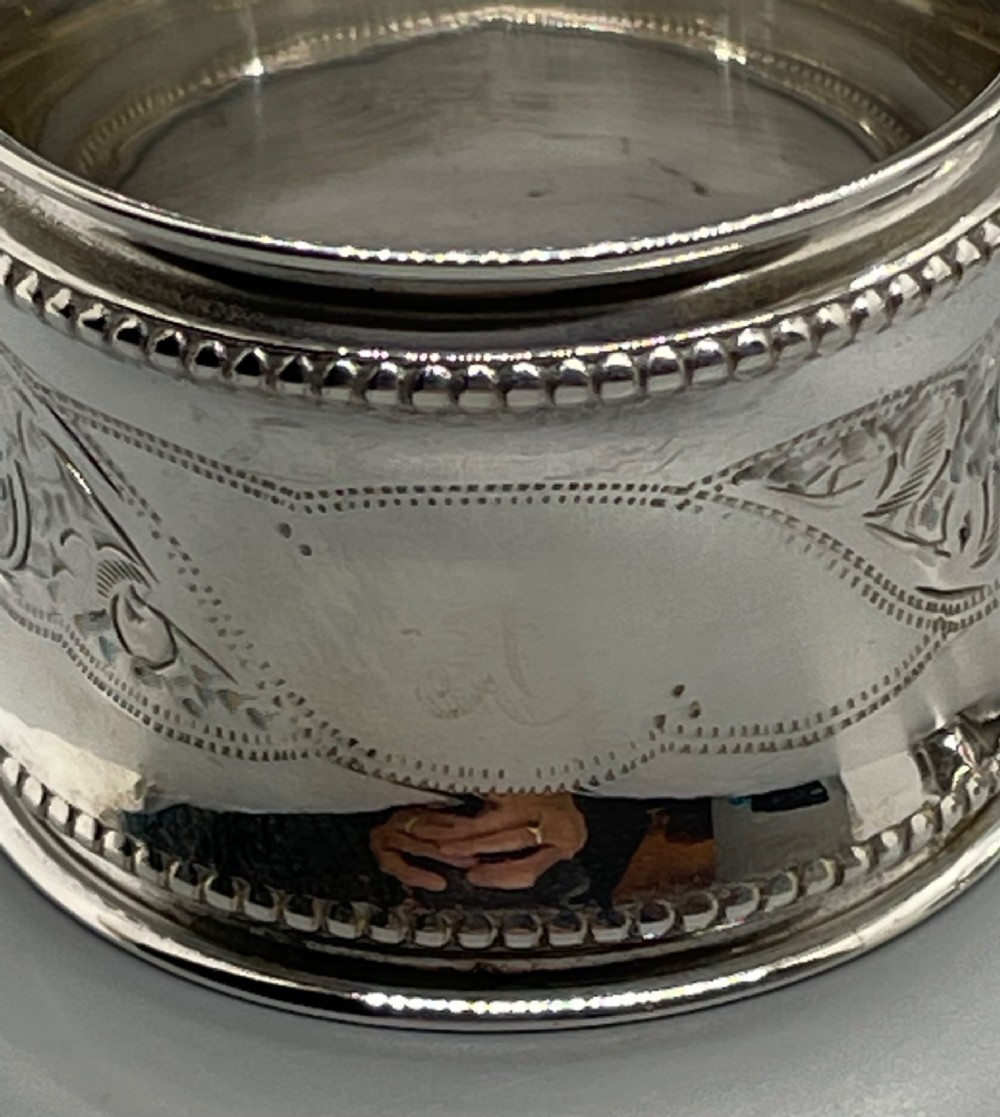 A set of six circular Edwardian sterling silver napkin rings with engraved patterns, displayed inside an open presentation box with green velvet lining. View X