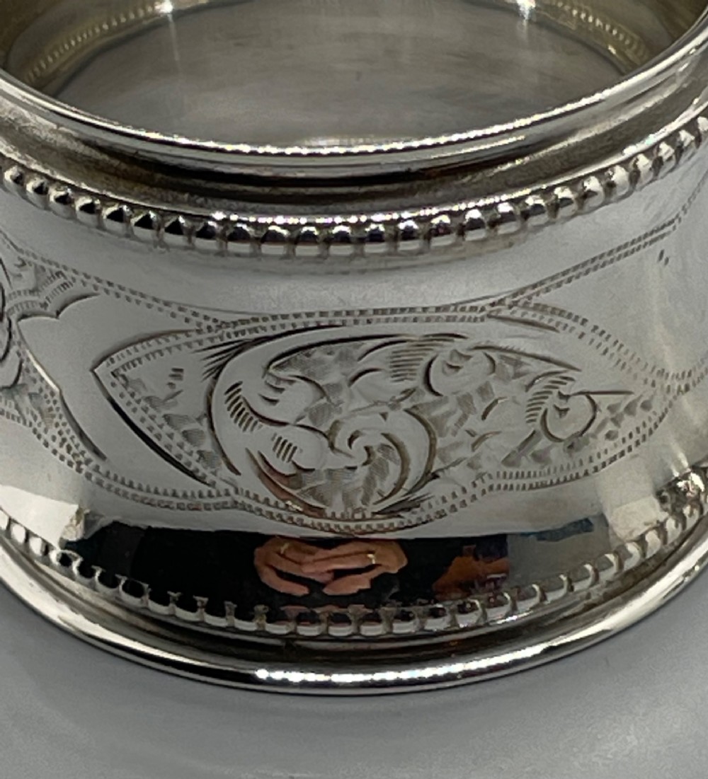 A set of six circular Edwardian sterling silver napkin rings with engraved patterns, displayed inside an open presentation box with green velvet lining. View XI