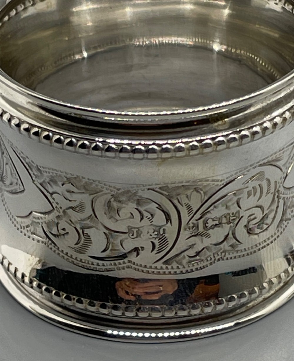 A set of six circular Edwardian sterling silver napkin rings with engraved patterns, displayed inside an open presentation box with green velvet lining. View XII