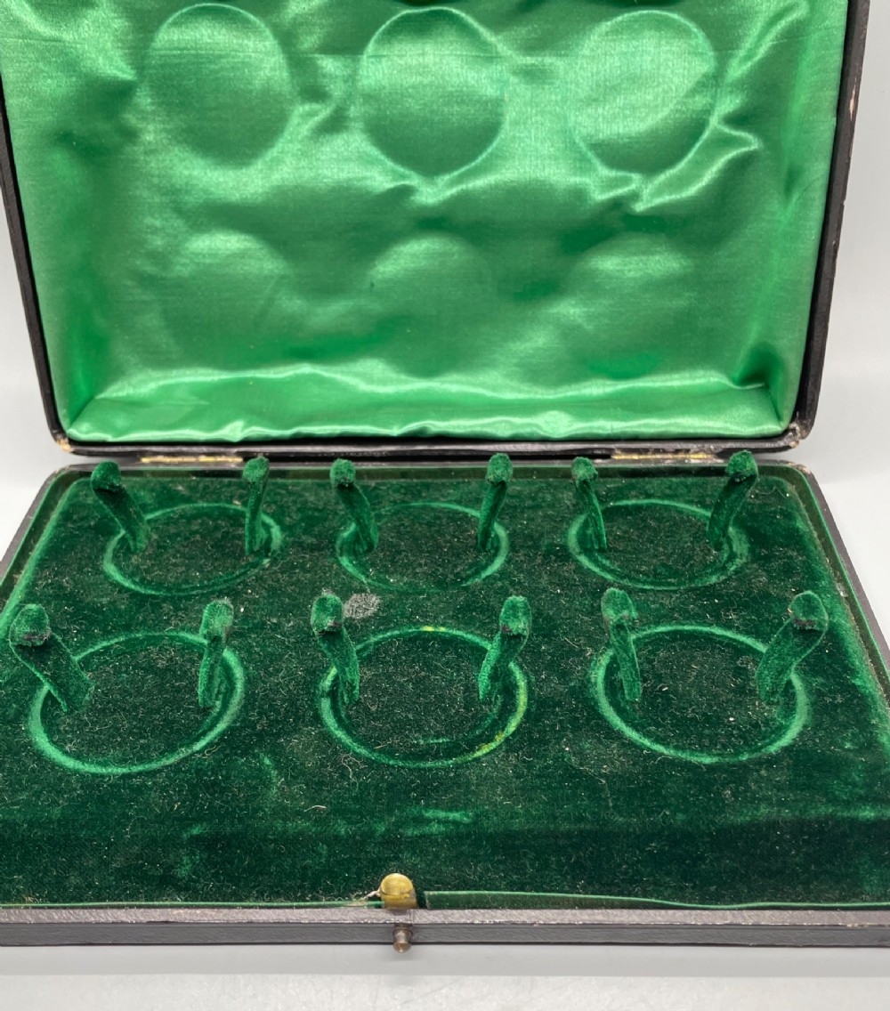 A set of six circular Edwardian sterling silver napkin rings with engraved patterns, displayed inside an open presentation box with green velvet lining. View XIII