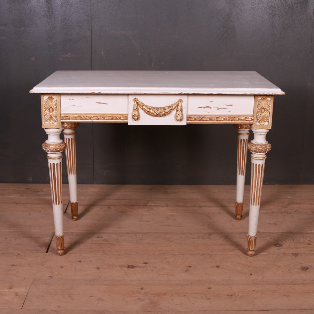 A Gustavian off-white painted writing table with gilded drapery swags, carved rosette blocks, and fluted legs.