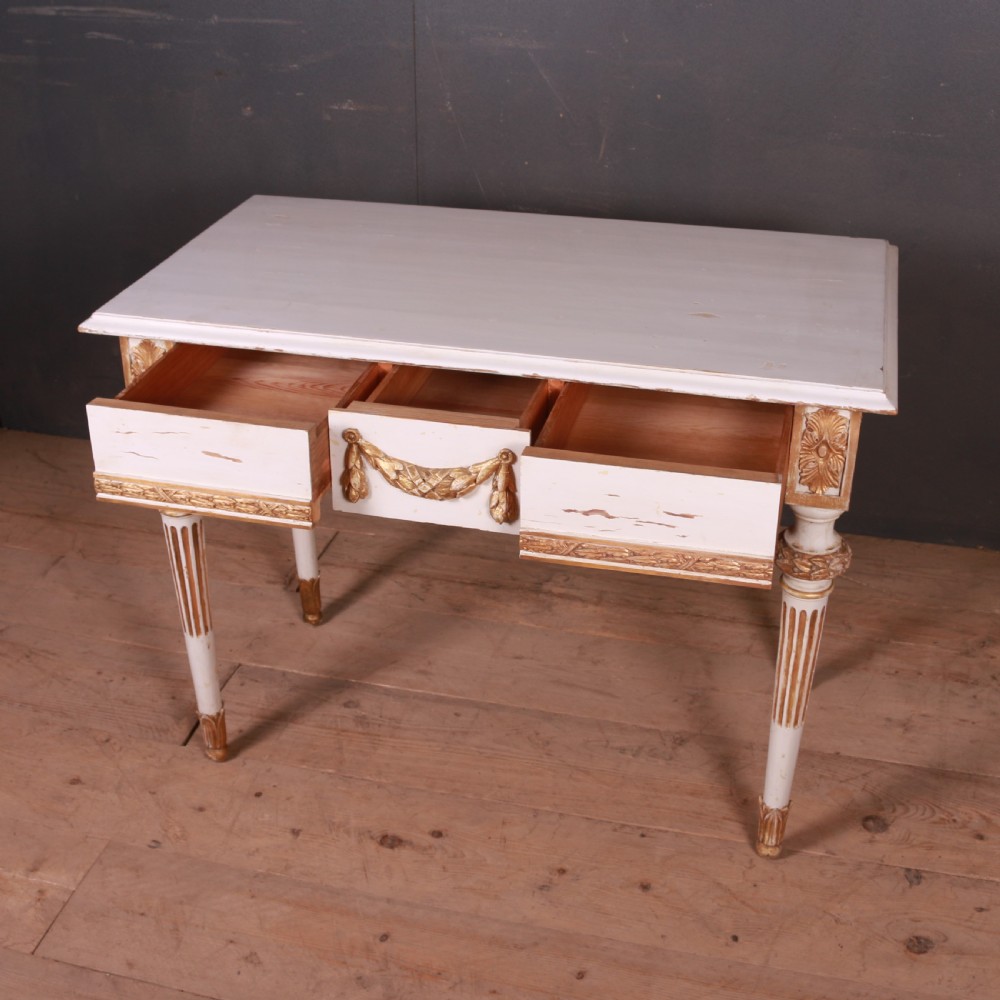 A Gustavian off-white painted writing table with gilded drapery swags, carved rosette blocks, and fluted legs. View VI