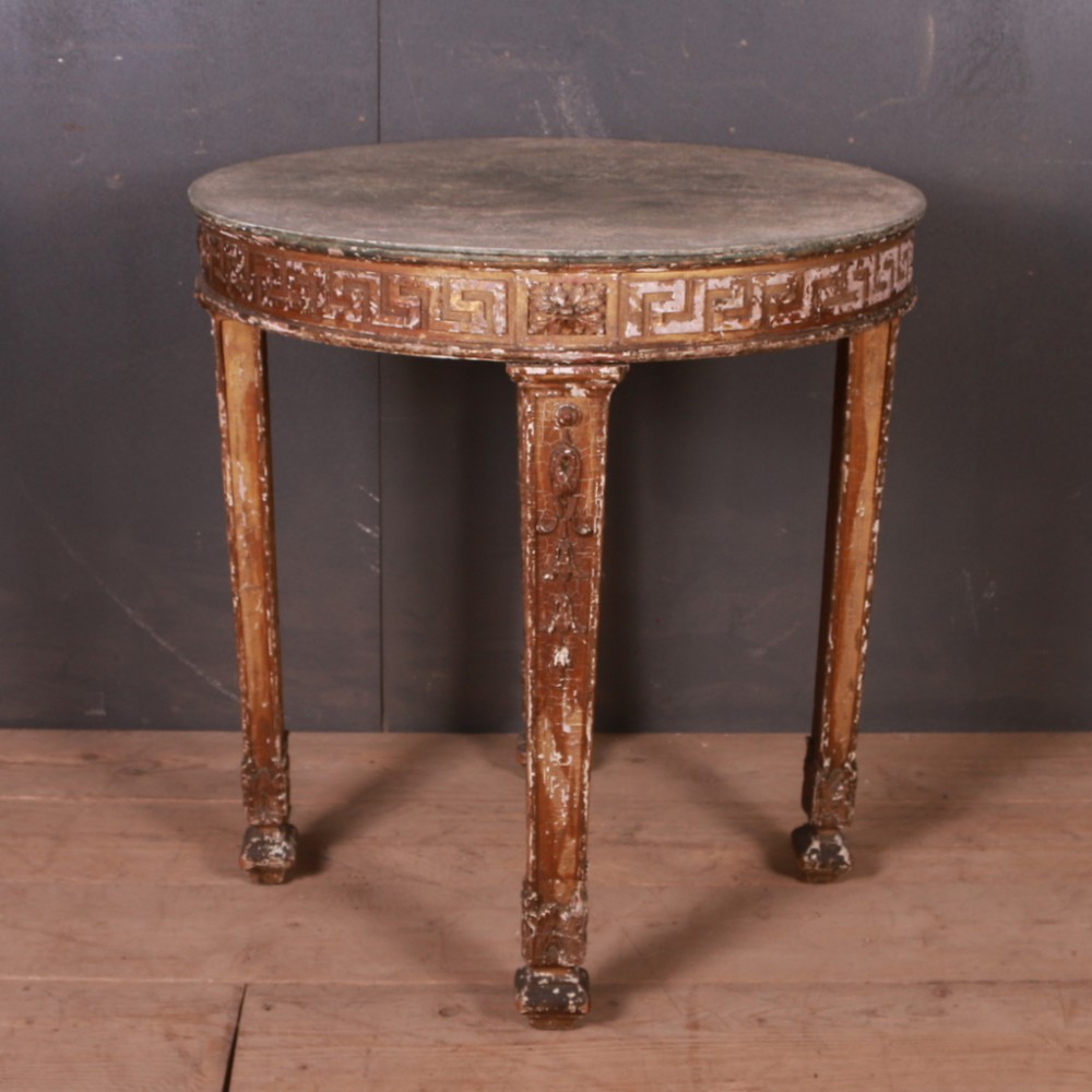 A circular antique Spanish painted lamp table featuring a carved Greek key frieze, tapered legs, and distressed gilded paintwork.