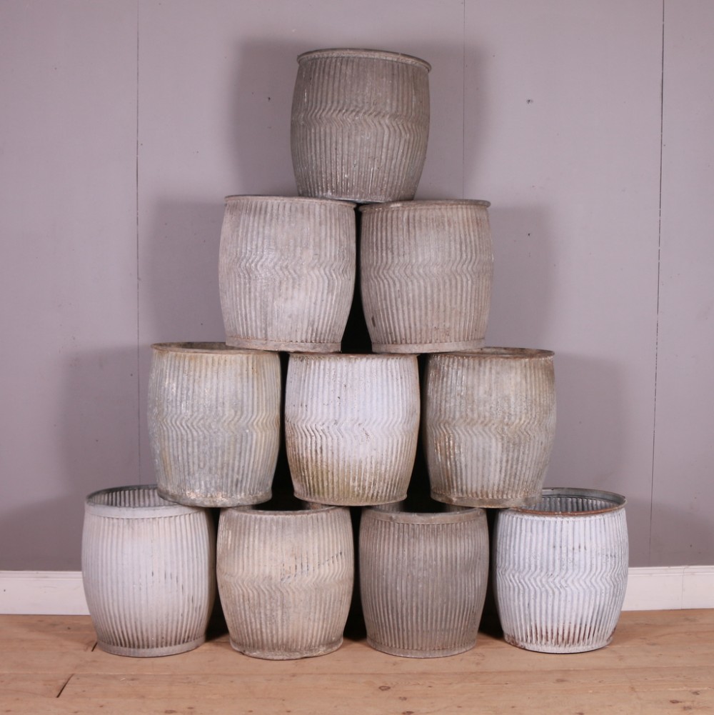 A stack of cylindrical corrugated zinc dolly tubs featuring vertical and chevron ribbed detailing.