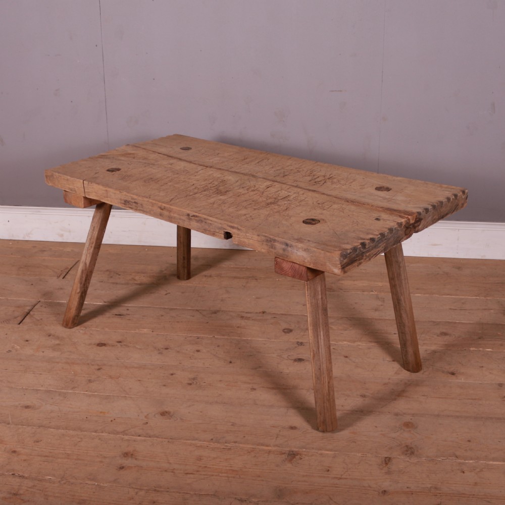 A rustic French scrubbed sycamore and elm trestle table featuring a thick plank top with visible peg construction and splayed wooden legs.