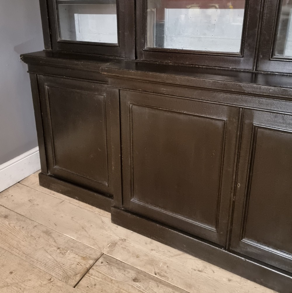 A large dark ebonised wooden breakfront library bookcase featuring glazed upper doors and panelled lower cupboard doors. View II