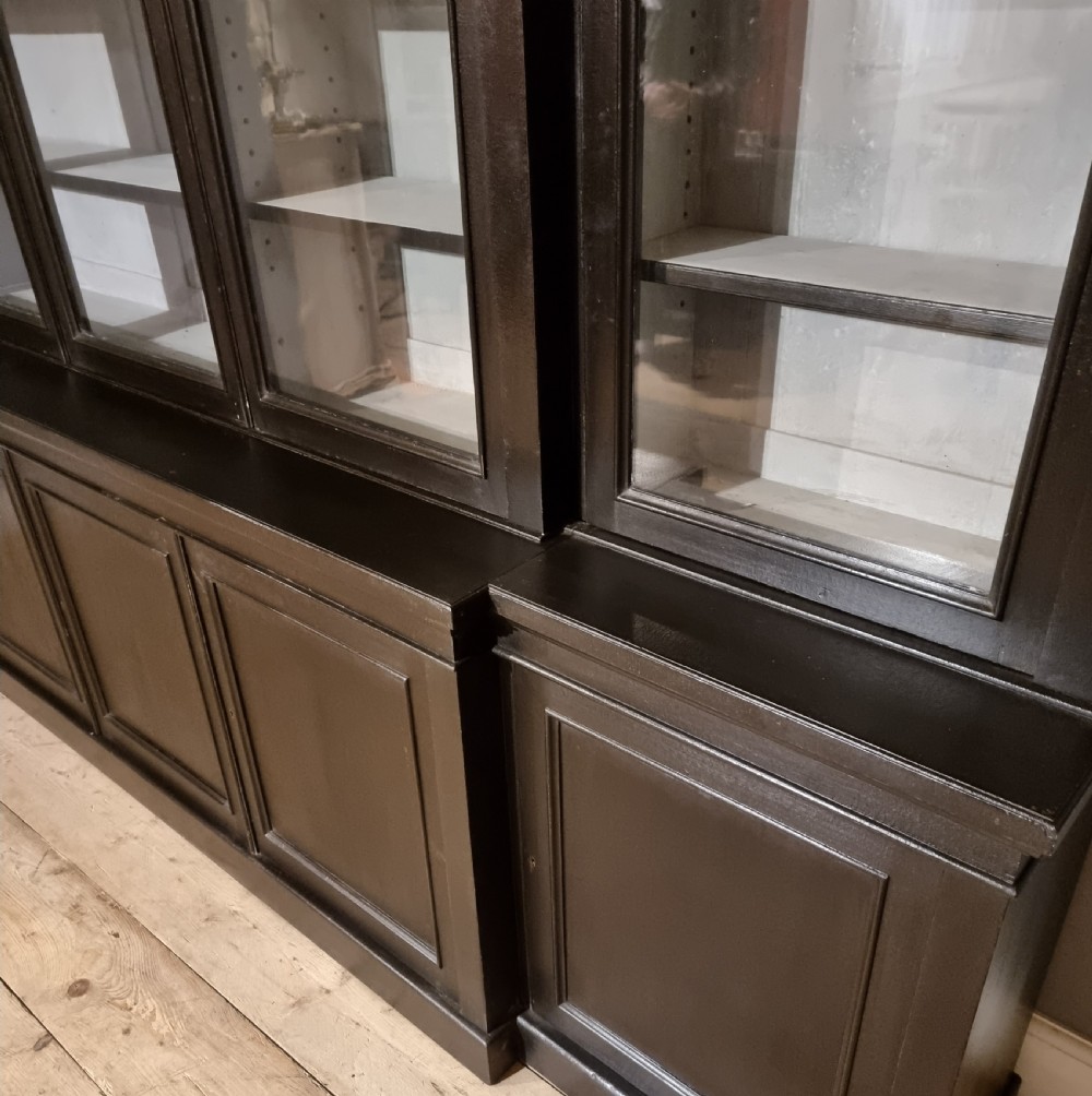 A large dark ebonised wooden breakfront library bookcase featuring glazed upper doors and panelled lower cupboard doors. View V