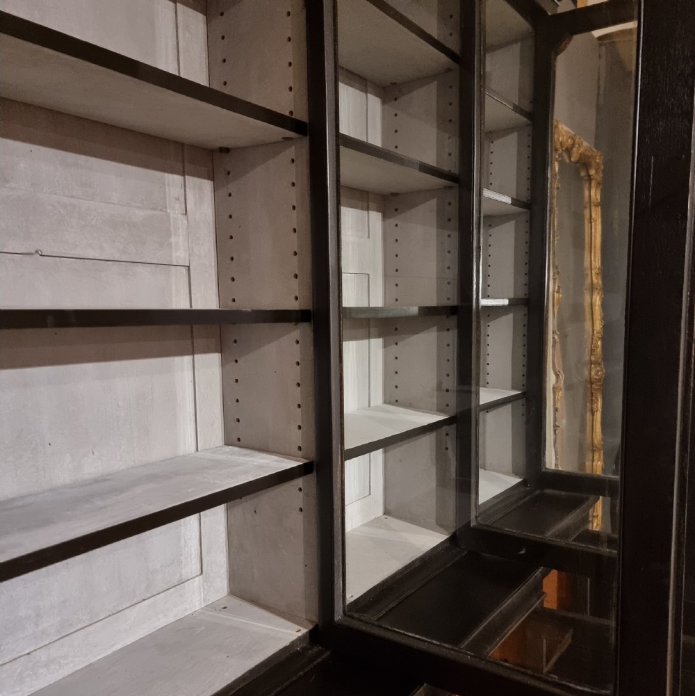 A large dark ebonised wooden breakfront library bookcase featuring glazed upper doors and panelled lower cupboard doors. View IX