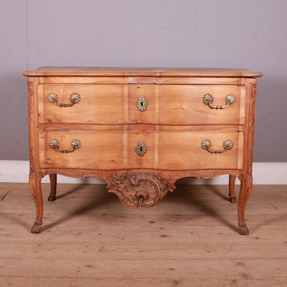 An eighteenth-century French serpentine timber chest of drawers featuring two drawer fronts, brass handles, and a centrally carved shell apron.