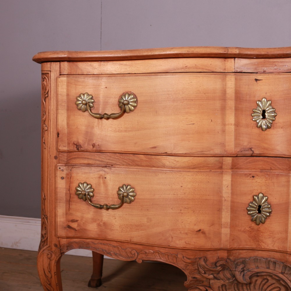 An eighteenth-century French serpentine timber chest of drawers featuring two drawer fronts, brass handles, and a centrally carved shell apron. View V