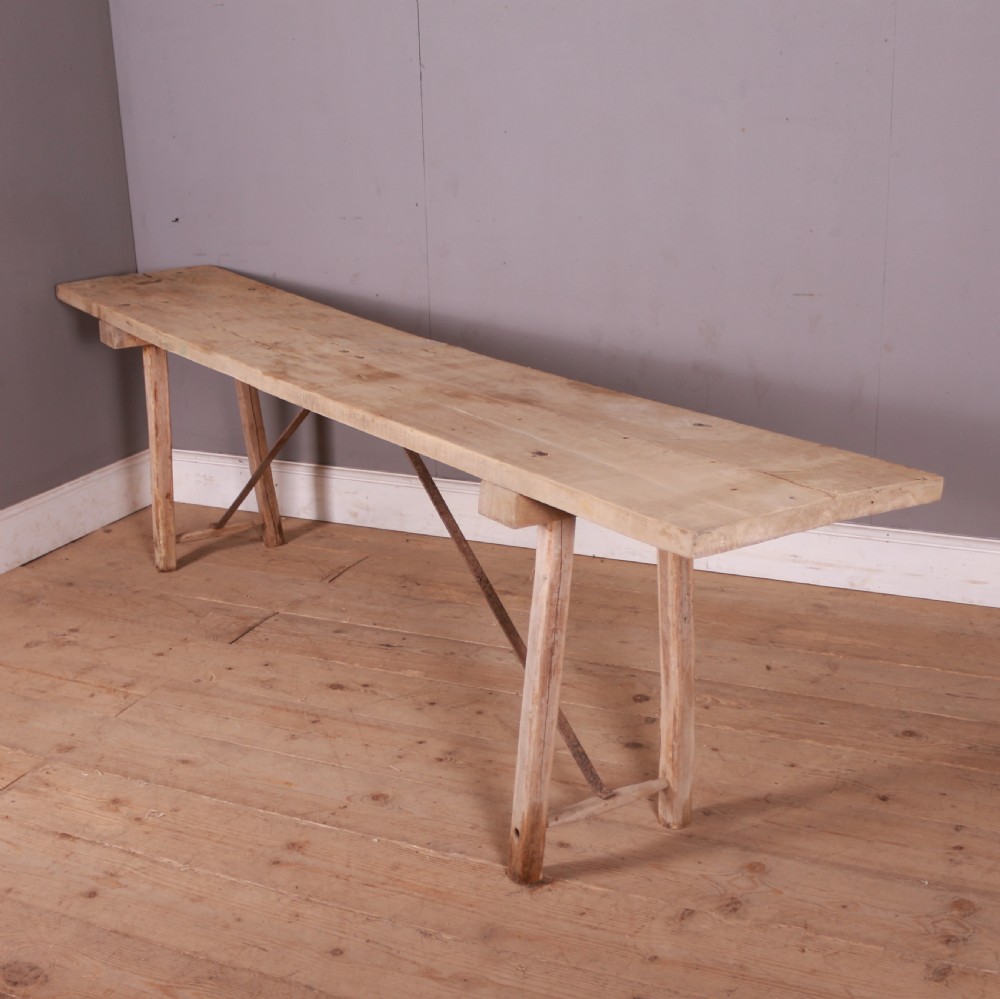 An elongated antique French trestle table made of scrubbed pale poplar wood with rustic A-frame legs and diagonal metal stretchers.