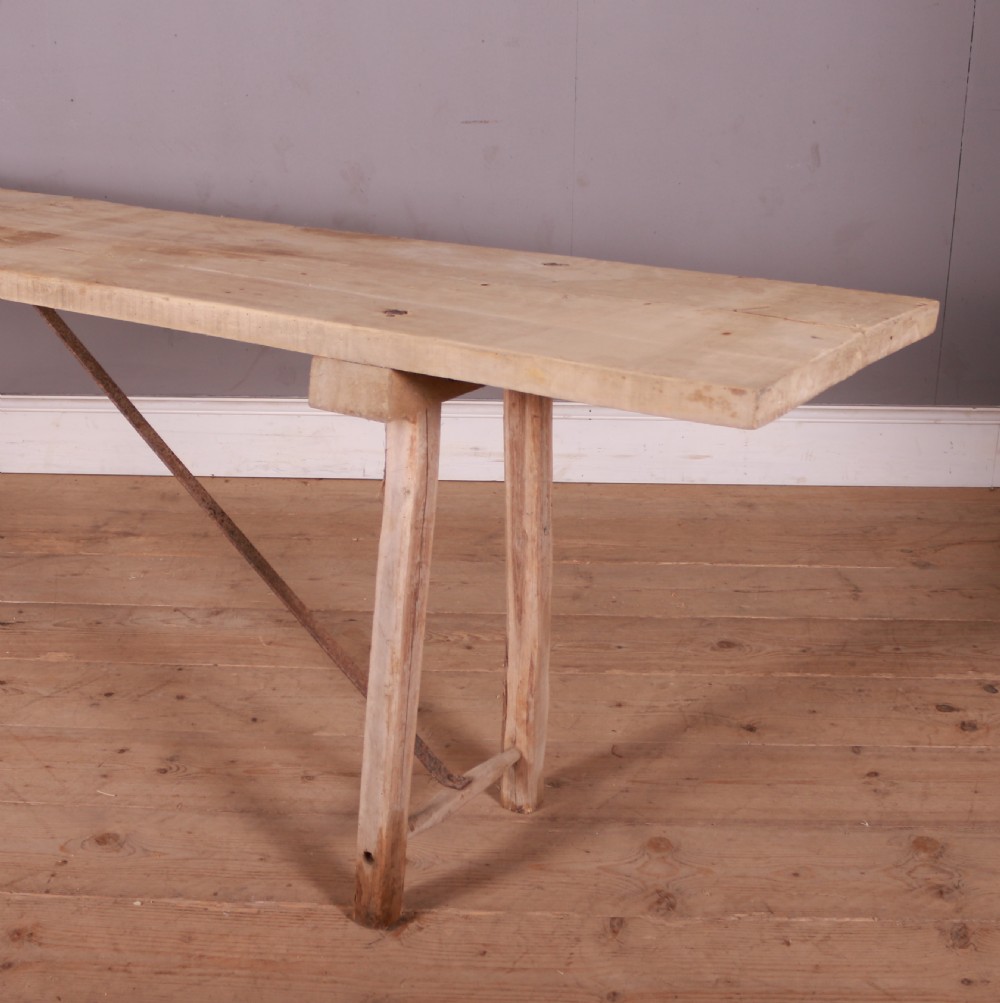 An elongated antique French trestle table made of scrubbed pale poplar wood with rustic A-frame legs and diagonal metal stretchers. View III