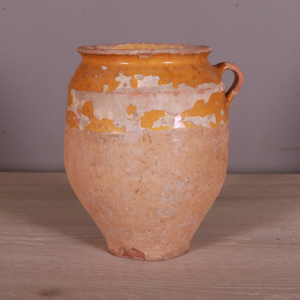 An antique French terracotta confit pot featuring an aged mustard-yellow glaze on the upper rim and a single side loop handle.