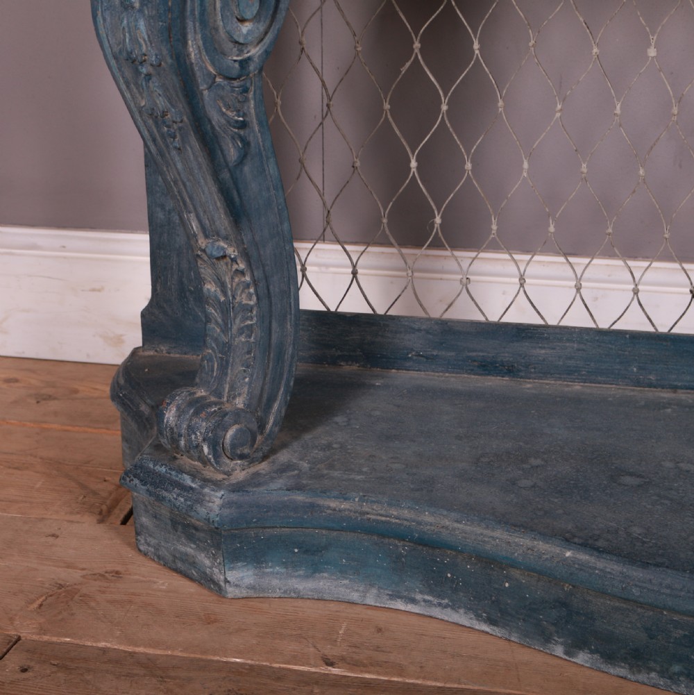 A French-style serpentine console table featuring a distressed blue painted finish, ornate carved scroll supports, a lower shelf, and a wire mesh back panel. View II