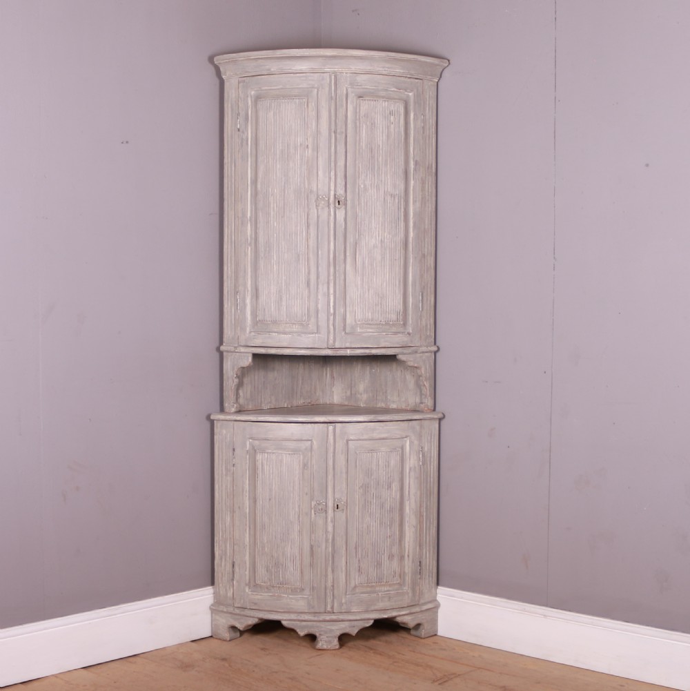 A tall antique Swedish bowfronted corner cupboard with a weathered grey painted finish, featuring panelled upper and lower doors and an open central niche.