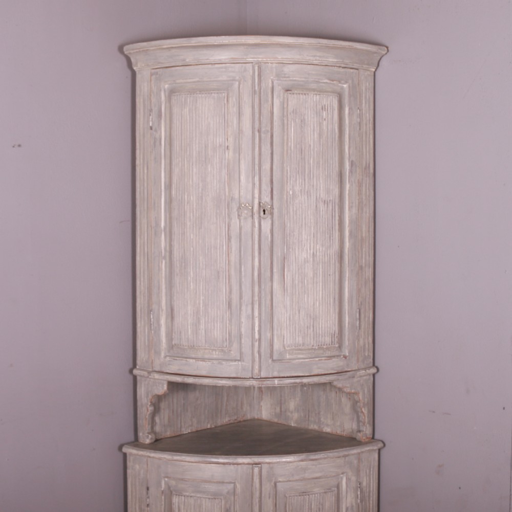 A tall antique Swedish bowfronted corner cupboard with a weathered grey painted finish, featuring panelled upper and lower doors and an open central niche. View II