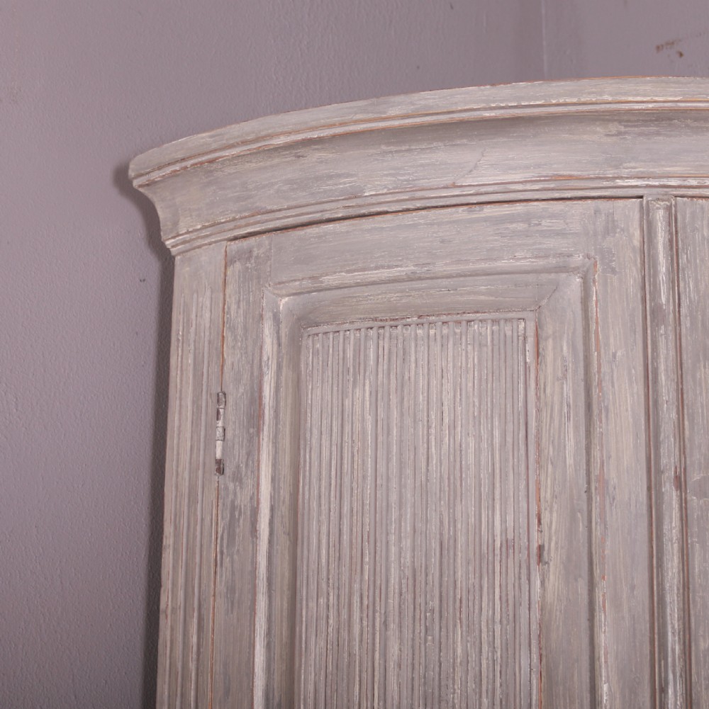 A tall antique Swedish bowfronted corner cupboard with a weathered grey painted finish, featuring panelled upper and lower doors and an open central niche. View IV