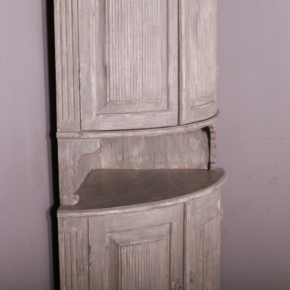 A tall antique Swedish bowfronted corner cupboard with a weathered grey painted finish, featuring panelled upper and lower doors and an open central niche. View V