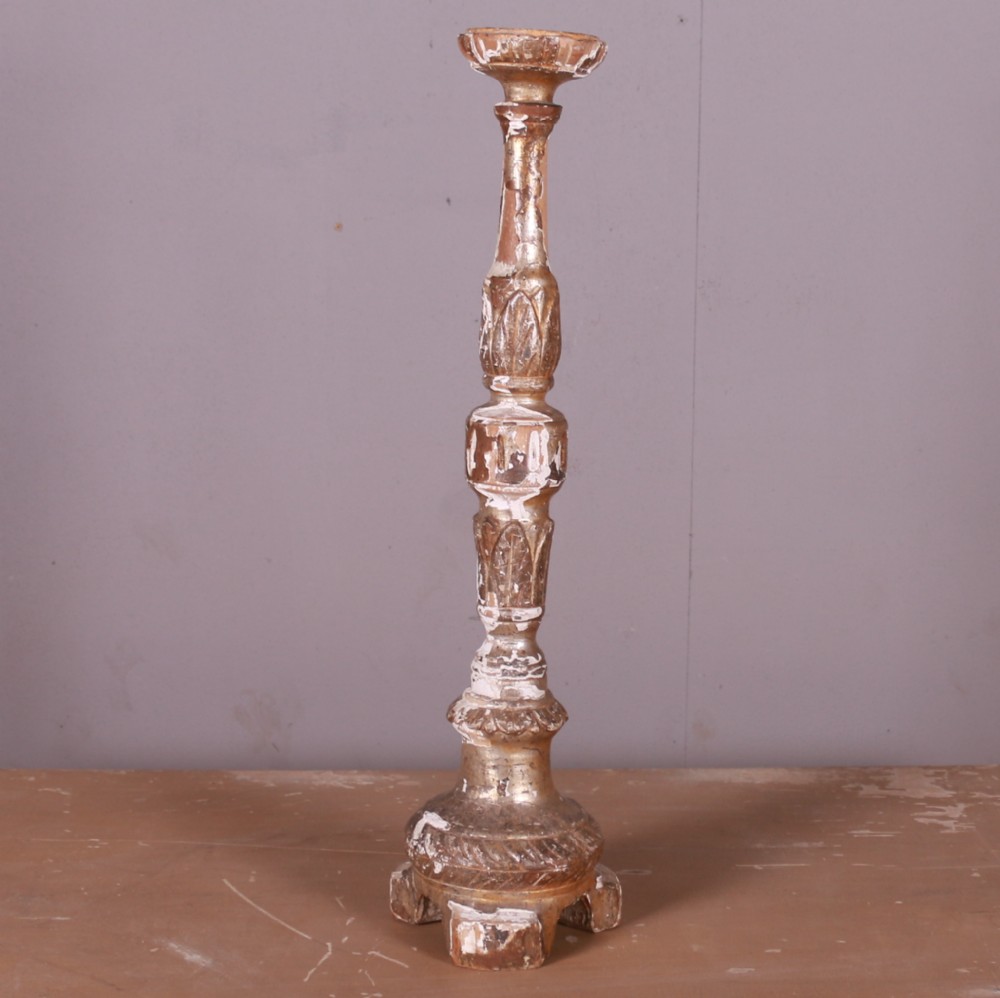 A tall hand-carved Italian giltwood candlestick featuring a turned shaft, leaf details, weathered gold finish over gesso, and a tripod base.