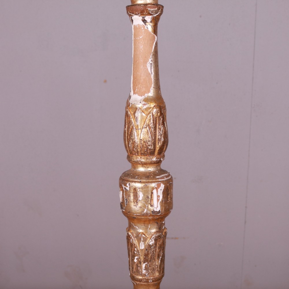 A tall hand-carved Italian giltwood candlestick featuring a turned shaft, leaf details, weathered gold finish over gesso, and a tripod base. View VII