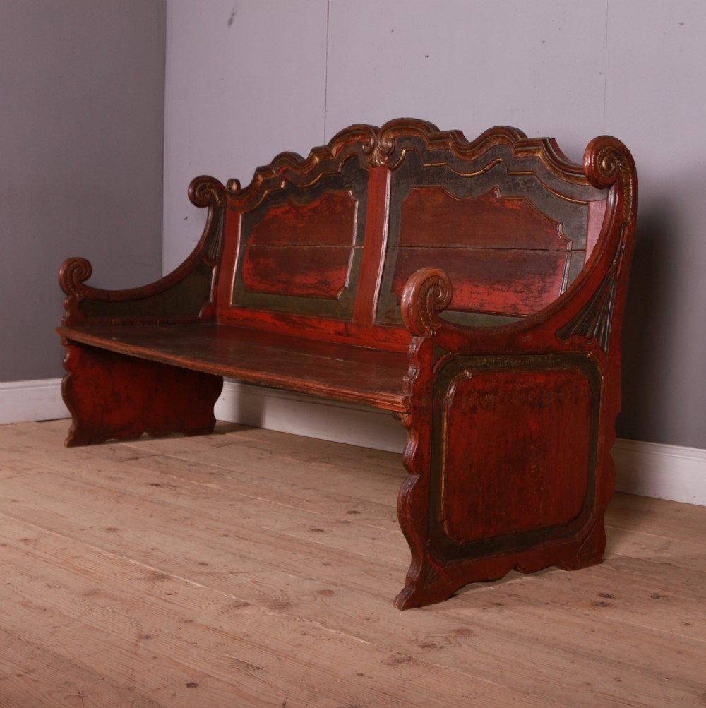An 18th-century Dutch painted wooden bench with a high serpentine back, scrolled arms, and red and dark green polychrome decoration.