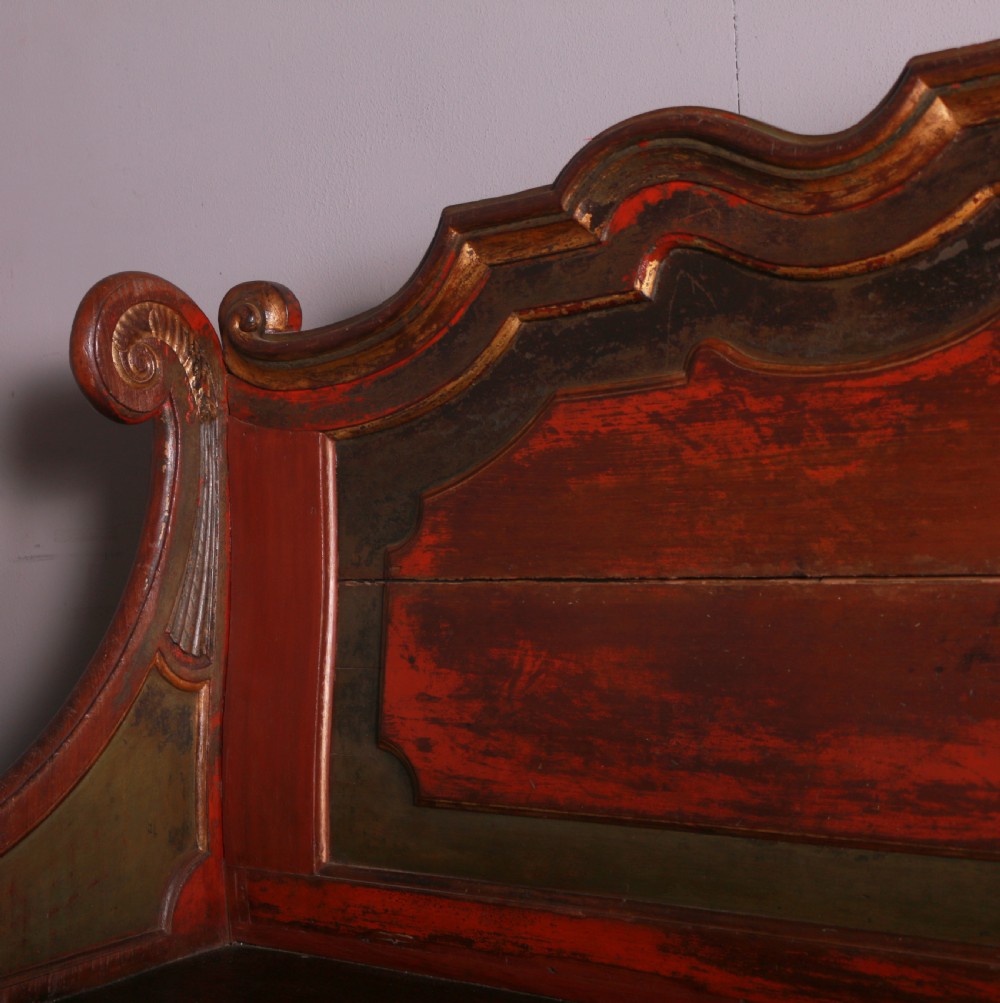 An 18th-century Dutch painted wooden bench with a high serpentine back, scrolled arms, and red and dark green polychrome decoration. View V