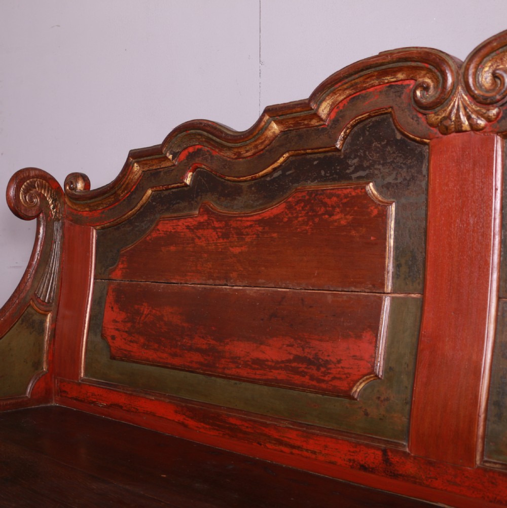 An 18th-century Dutch painted wooden bench with a high serpentine back, scrolled arms, and red and dark green polychrome decoration. View VIII