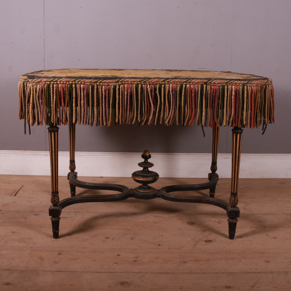 A 19th-century French ebonised centre table featuring fluted legs with gilt accents, a curved stretcher with a turned finial, and a floral tapestry top surrounded by long fringe. View II