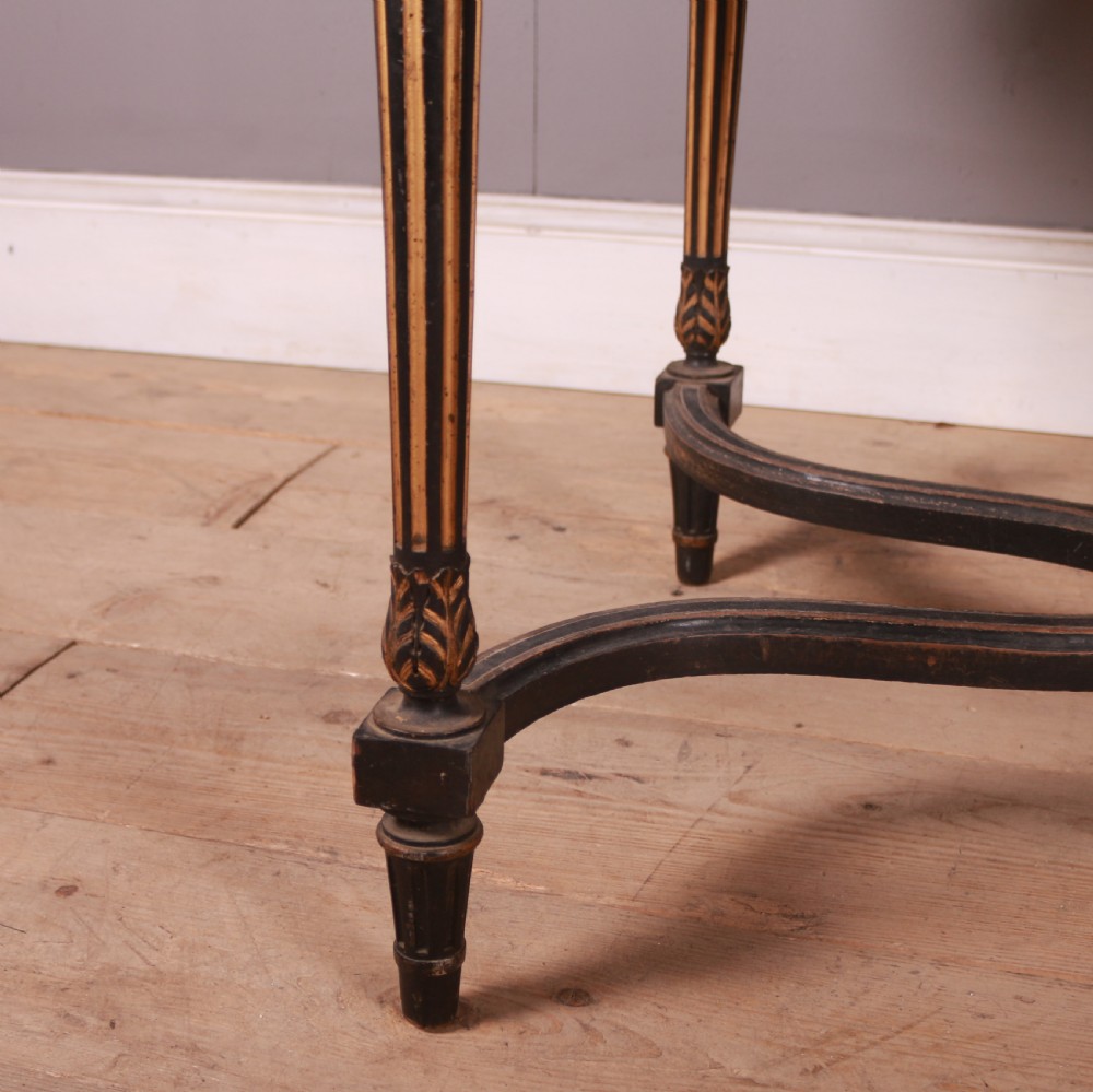 A 19th-century French ebonised centre table featuring fluted legs with gilt accents, a curved stretcher with a turned finial, and a floral tapestry top surrounded by long fringe. View IV