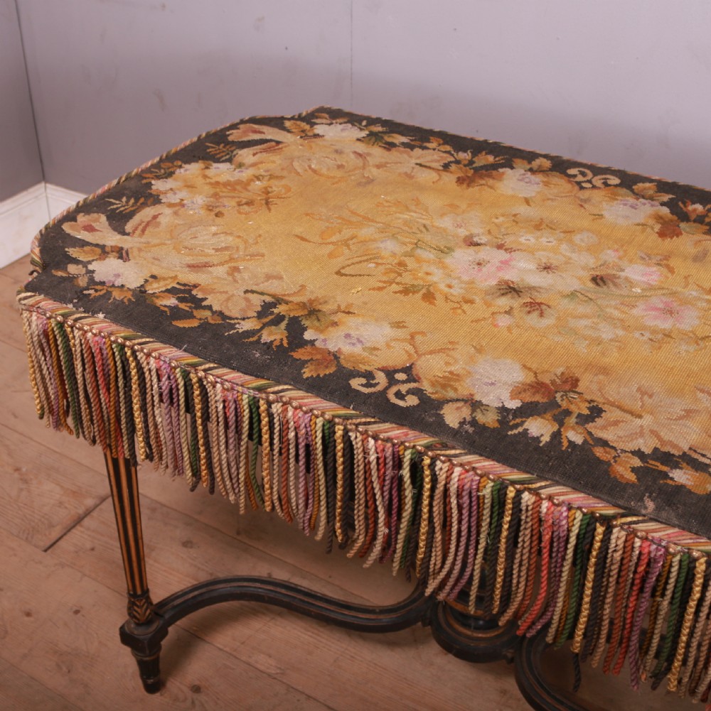 A 19th-century French ebonised centre table featuring fluted legs with gilt accents, a curved stretcher with a turned finial, and a floral tapestry top surrounded by long fringe. View V