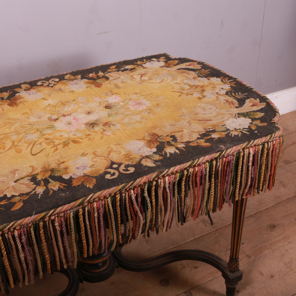 A 19th-century French ebonised centre table featuring fluted legs with gilt accents, a curved stretcher with a turned finial, and a floral tapestry top surrounded by long fringe. View VI