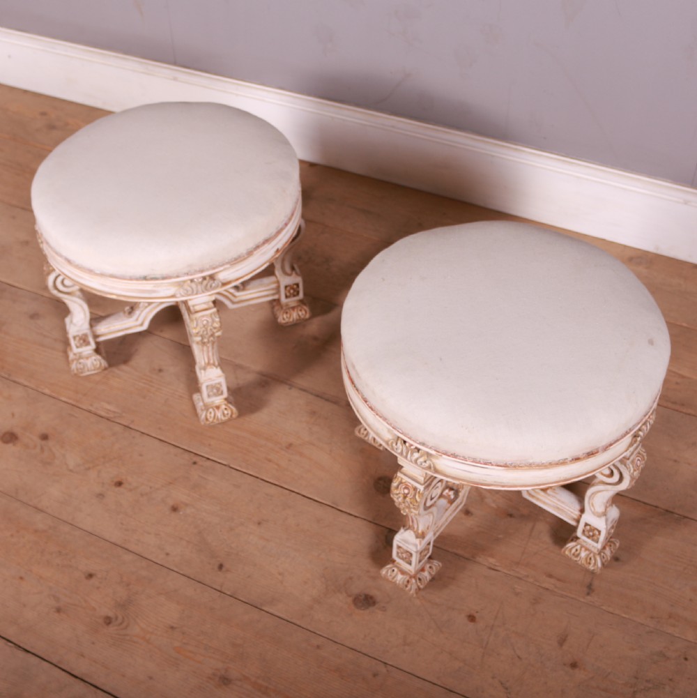 A pair of circular Swedish stools featuring cream and gold painted frames, scroll legs, arched stretchers, and off-white upholstered seats. View VI