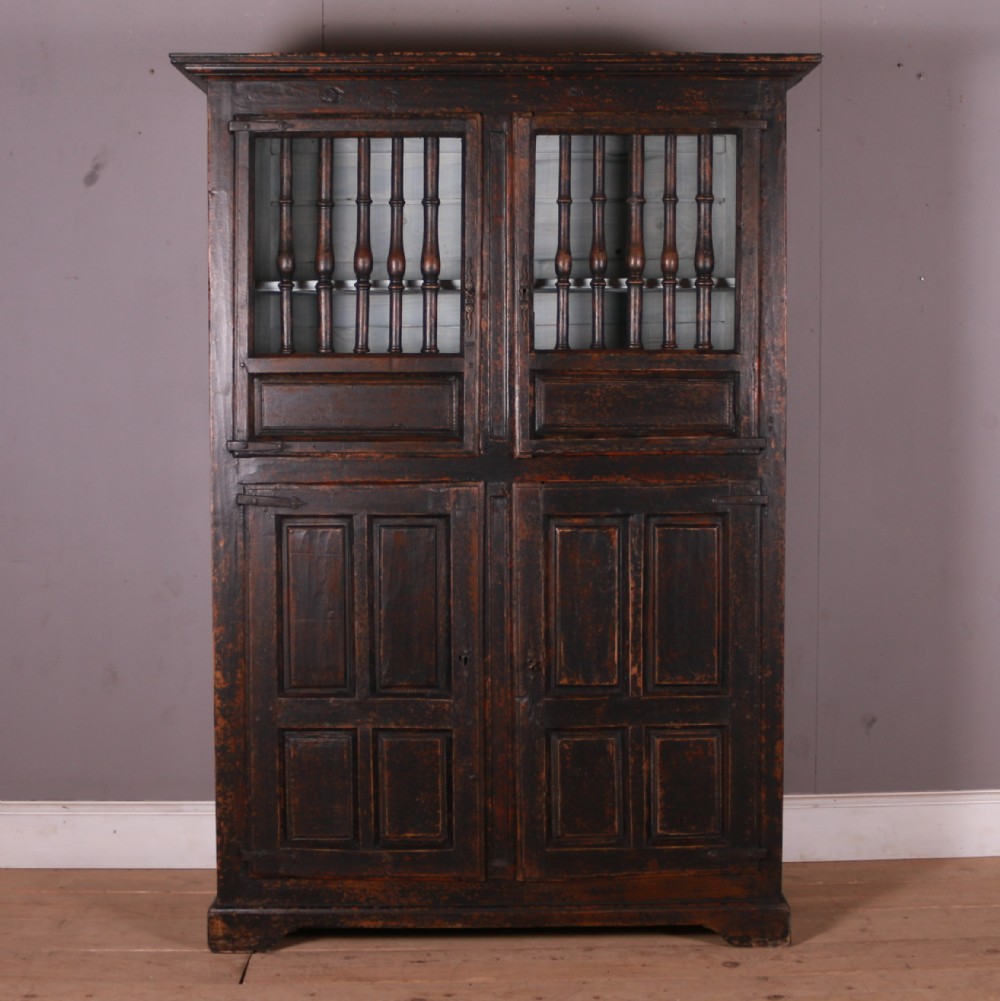 An 18th-century French dark oak food cupboard featuring turned spindle upper door panels and solid wooden lower door panels.