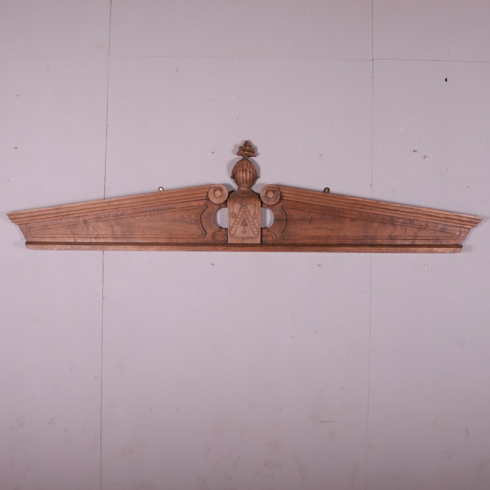 A hand-carved oak architectural door pediment featuring a central helmet crest with scroll volutes and sloping moulded sides.