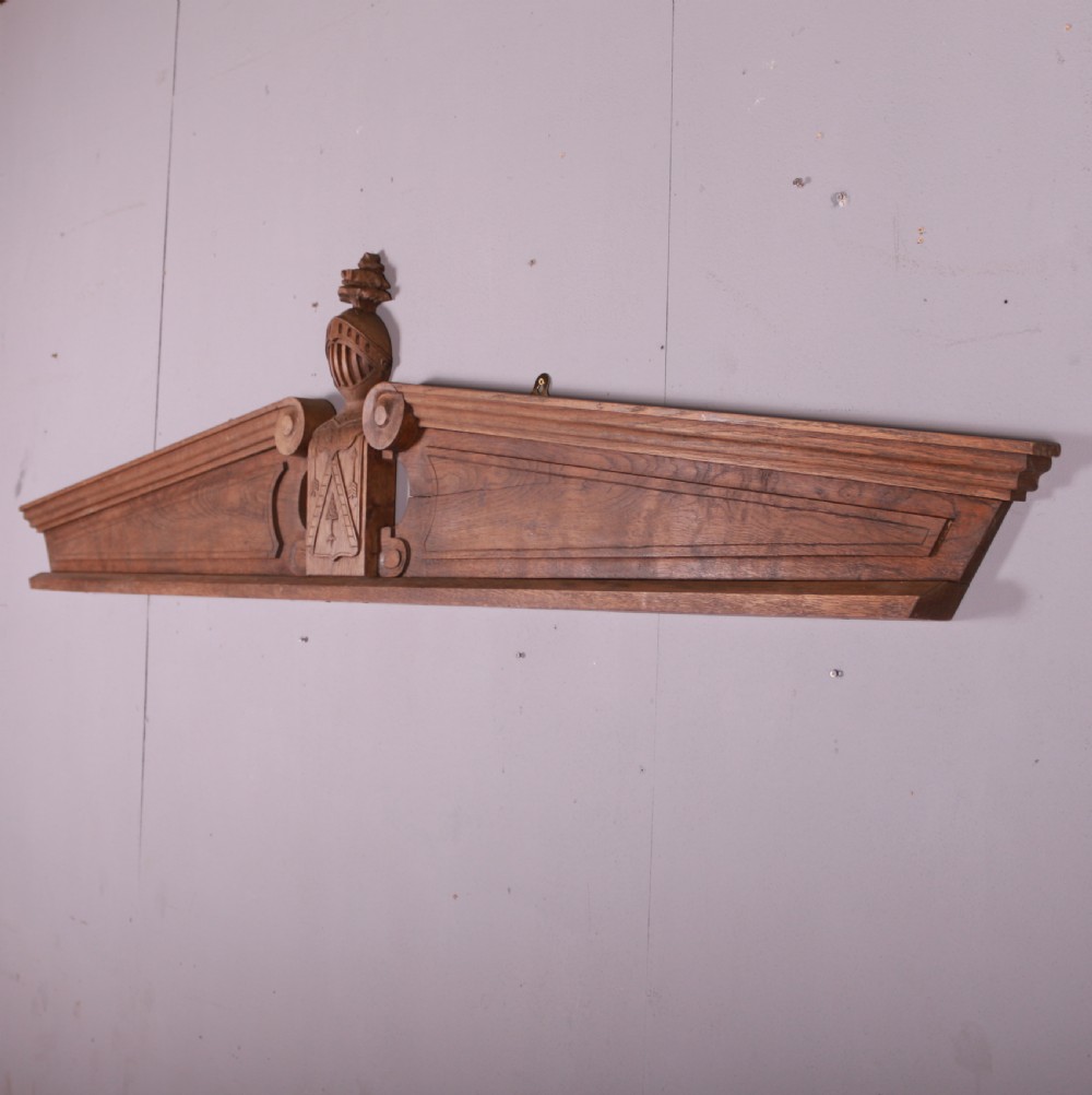 A hand-carved oak architectural door pediment featuring a central helmet crest with scroll volutes and sloping moulded sides. View III