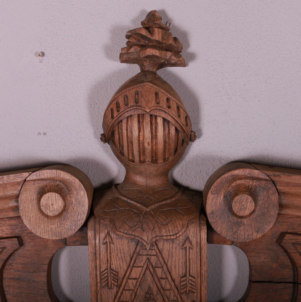 A hand-carved oak architectural door pediment featuring a central helmet crest with scroll volutes and sloping moulded sides. View IV