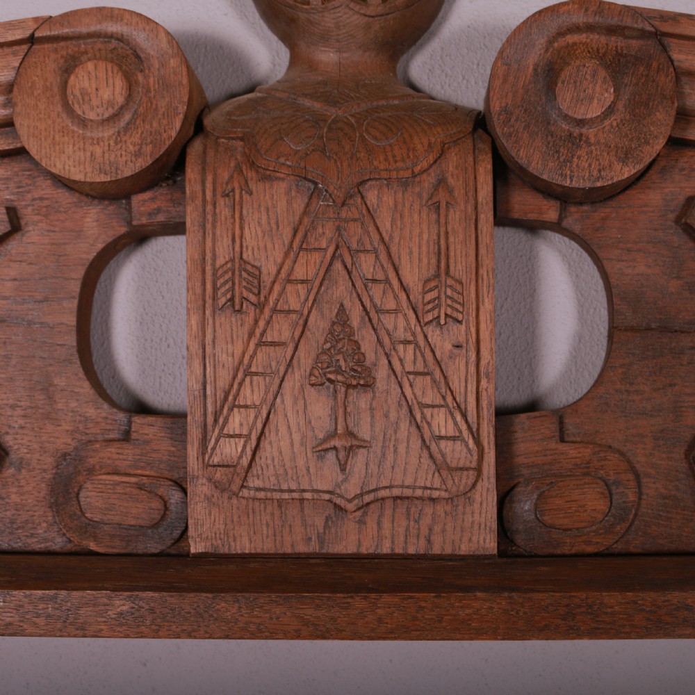 A hand-carved oak architectural door pediment featuring a central helmet crest with scroll volutes and sloping moulded sides. View V