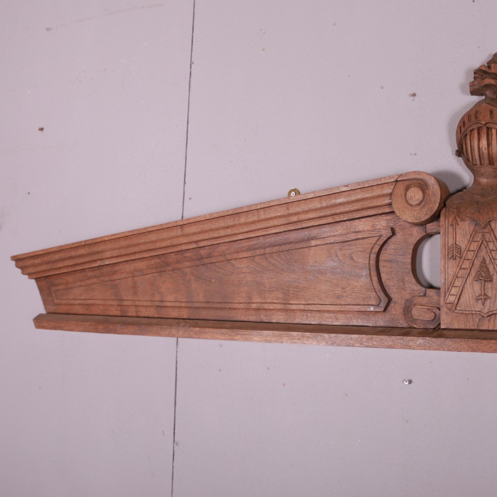 A hand-carved oak architectural door pediment featuring a central helmet crest with scroll volutes and sloping moulded sides. View VI