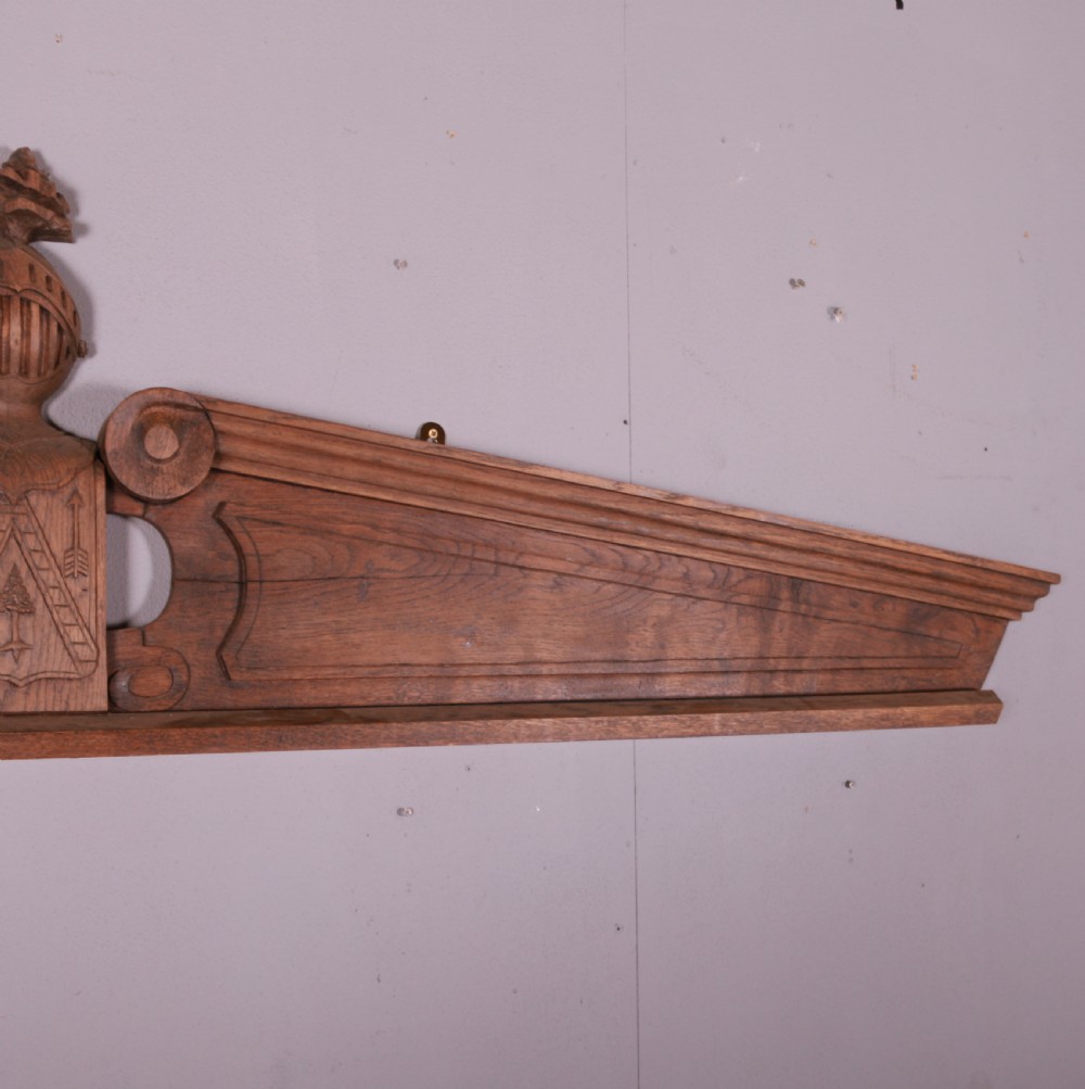 A hand-carved oak architectural door pediment featuring a central helmet crest with scroll volutes and sloping moulded sides. View VII