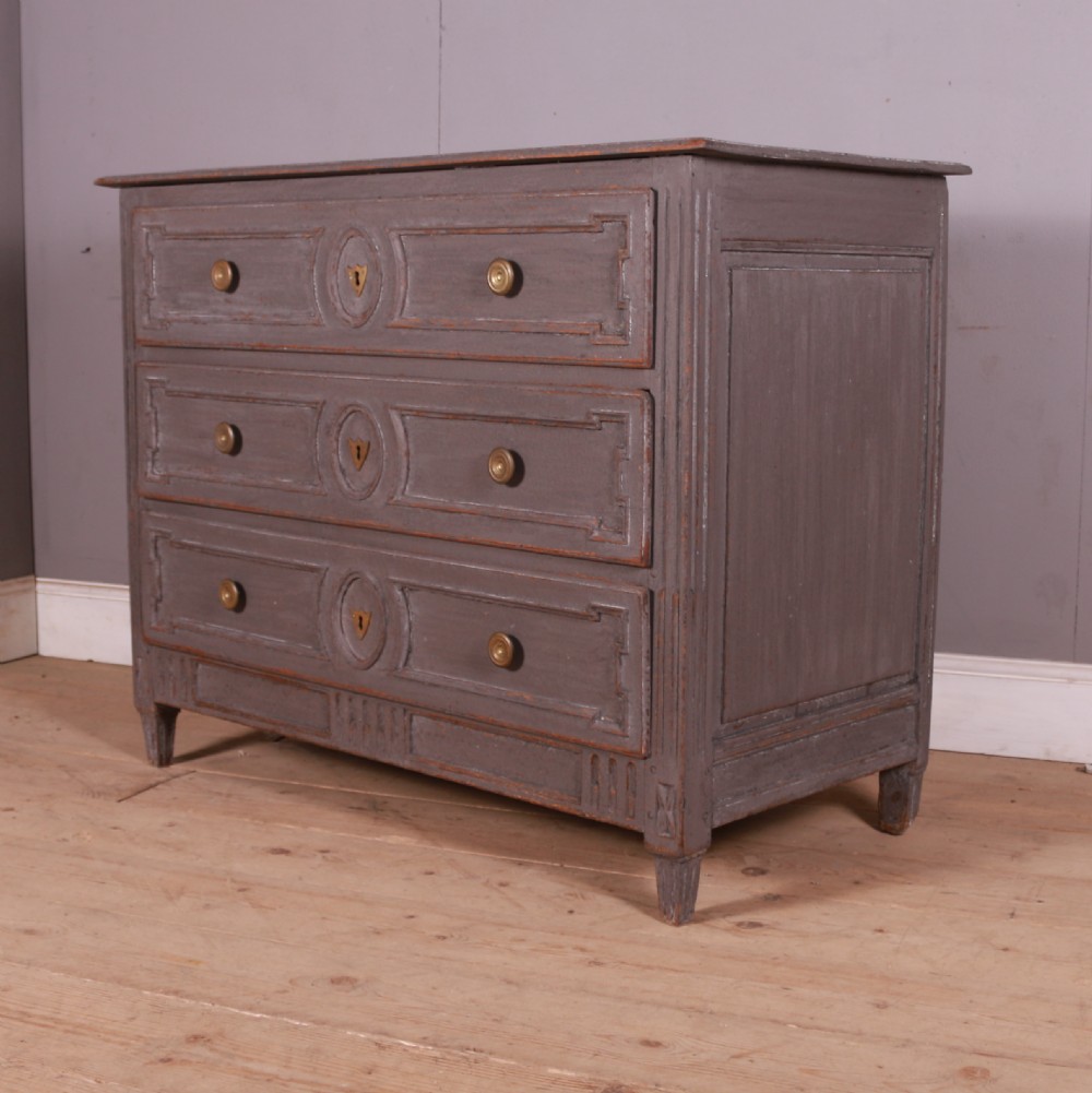 A French Neoclassical grey-painted three-drawer commode featuring geometric drawer moldings, brass hardware, and fluted legs.