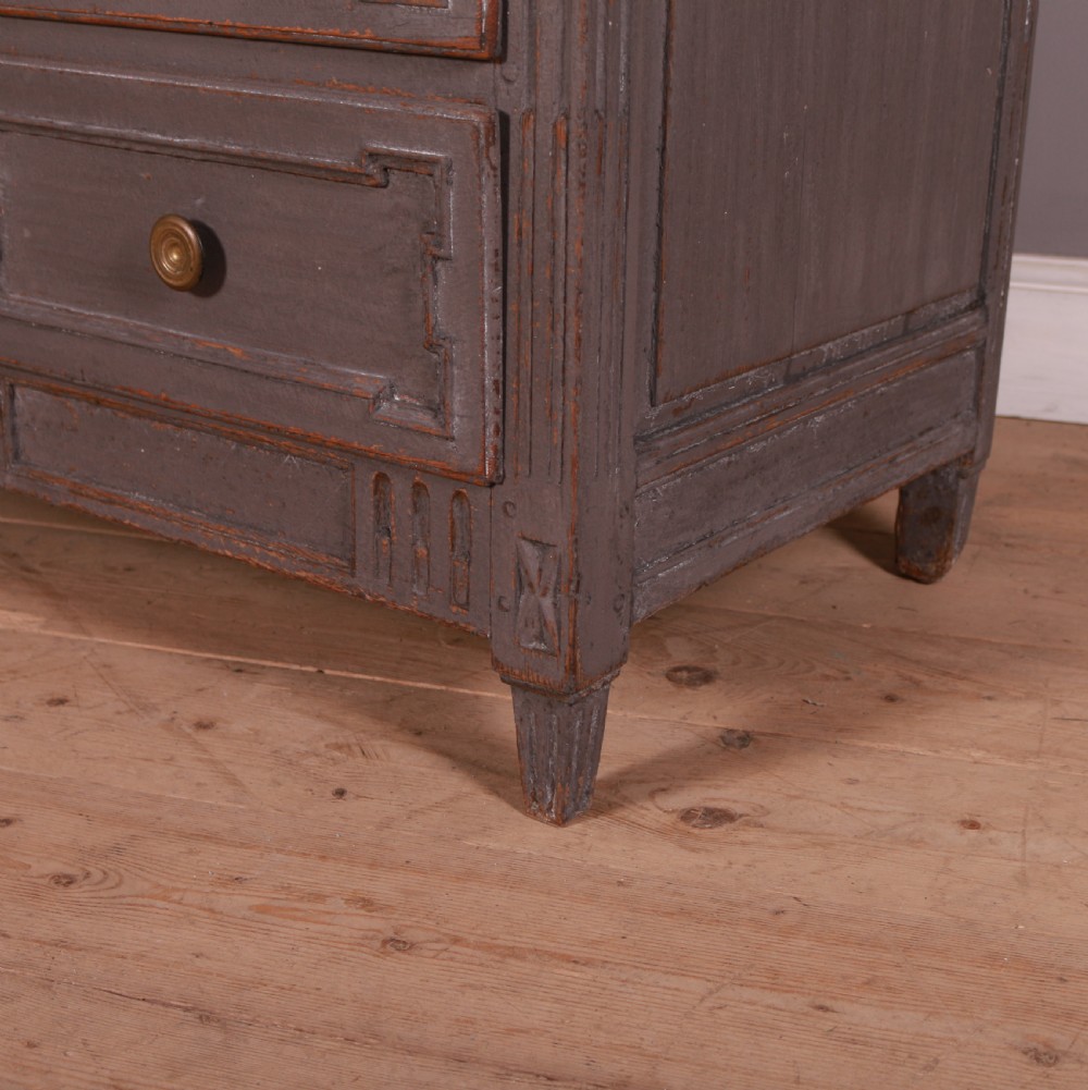 A French Neoclassical grey-painted three-drawer commode featuring geometric drawer moldings, brass hardware, and fluted legs. View II